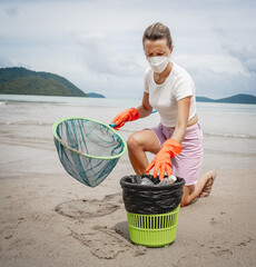 A female ecologist volunteer cleans the beach on the seashore from plastic and other waste