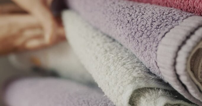 Women's fingers sort through clean towels on a shelf in the closet