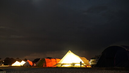 Fototapeta na wymiar Leuchtende Zelte auf Campingplatzt mit Dramatischem Nachthimmel