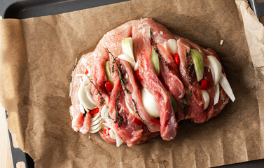 A large piece of raw pork meat prepared for baking, with onions and spices and thyme on parchment...