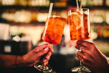 woman hands at the bar clink glasses with cocktails