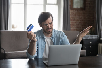 Annoyed frustrated bank customer man using laptop, reading message, notice about problem with credit card, blocked account, counting expenses, loss, getting financial overspending, bankruptcy - obrazy, fototapety, plakaty