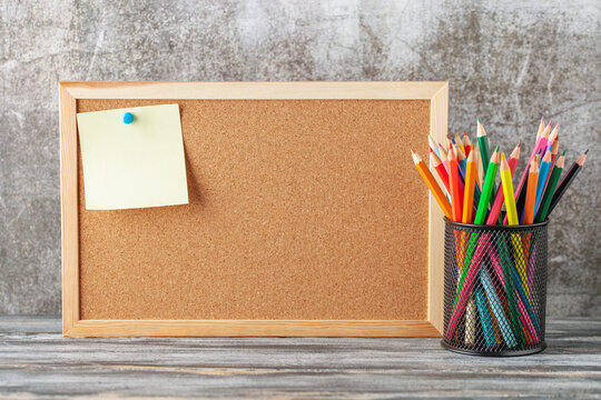 Back to school concept. A cork board with a paper sheet for recording, and a basket of colored pencils
