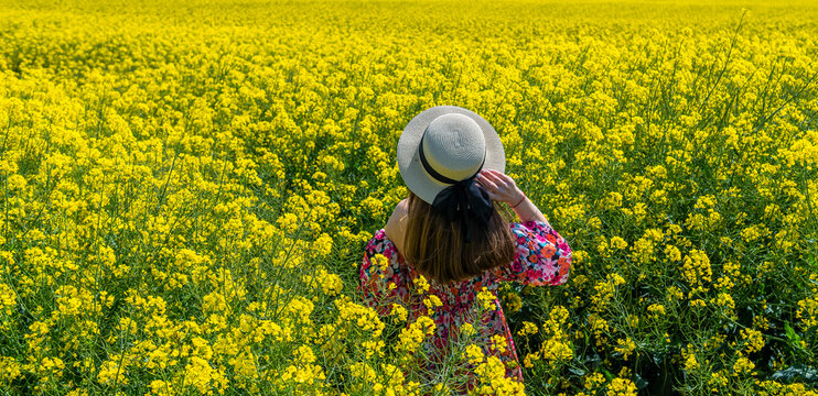 Beautiful girl with dress and hat in the Canola Fields. Blooming canola fields under a blue sky with clouds. Beautiful yellow flowers. Happy girl in nature.