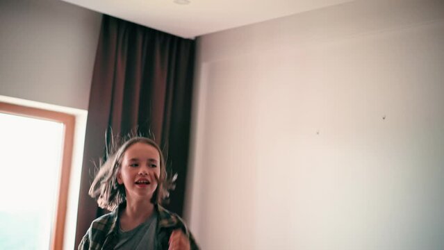 A caucasian eight-year-old girl having fun jumping and dancing on the bed while listening to music.