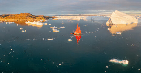 Sail boat with red sails cruising among ice bergs during dusk in front of a full moon. Disko Bay, Greenland.
Midnight sun, romantic view.
Climate change and global warming
