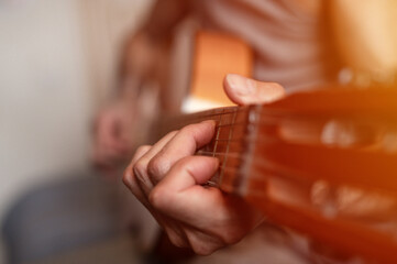 male hands of an elderly senior caucasian man holding and playing a classical guitar close up at home. unprofessional faceless guitarist people play amateur music. domestic hobbies and leisure. flare