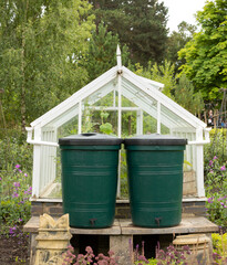 Obraz premium Two green water butts outside a greenhouse being used for water storage, water collection system in place, eviromental concept