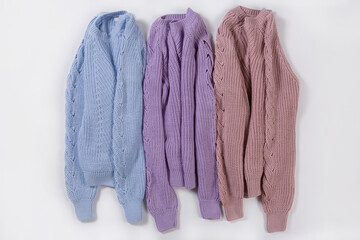 Three knitted sweaters in pastel colors, lying side by side on a white background