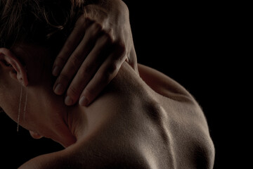 female back on a dark background, hands on the neck with cervical osteochondrosis