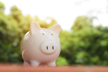 Money saving concept. White piggy bank was placed on the table with blurred bokeh outdoor green...