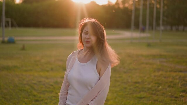 Smiling lady in unbuttoned shirt shakes loose hair on field at sunset slow motion. Enjoying warm summer evening. Freedom and active lifestyle