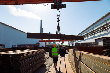 Worker transporting stack of metal pipes with gantry crane