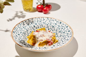 Italian ravioli with spinach, cheese and tomato in ceramic plate on white table. Cheese ravioli with creamy espuma and tomato. Italian ravioli with spinach and cheese filled and creamy topped.