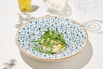 Traditional italian food - cheese risotto with arugula on ceramic plate. Cheese risotto with parmesan and rucola on sunny day. Classic risotto milanese with cheese. Italian food - creamy rice.