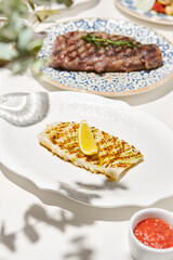 Grilled calamari on light background with shadows. Grilled squid with lemon on white table. Aesthetic composition with bbq squid. Bbq calamari. Grilled seafood. Summer menu.