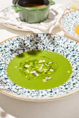 Composition with vegetable soup in ceramic bowl. Green soup with broccoli and cheese on summer day. Italian soup with green pea. Vegan menu. Hot dishes. Vegetables food. Eat less meat.