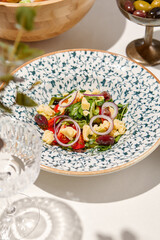 Traditional italian food - panzanella salad with tomatoes, onion rings and croutons. Panzanella salad on white table in summer menu. Composition with Tomato salad and glasses in sunny day.