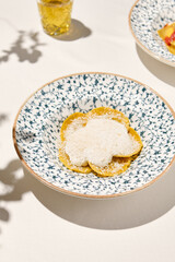 Italian ravioli with cheese and creamy sauce in ceramic plate on white table sunny day. Cheese ravioli with creamy espuma and parmesan. Italian ravioli with quattro formaggi filled 