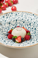 Classic panna cotta with berries on light background. Italian dessert from milk jelly - panna cotta. Desserts menu. Aesthetic composition with panna cotta and strawberries, raspberry and blueberry.