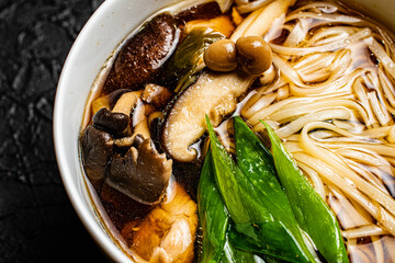 Mushroom soup udon noodles with fresh green onions in a fine white bowl against a black design board, a traditional Japanese meal.