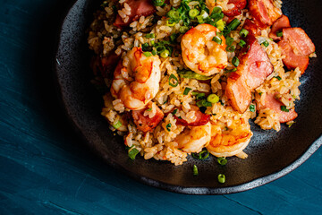 Fried rice with bacon and shrimp against a blue plaster design board. 