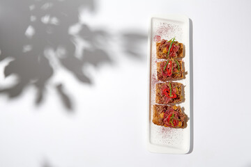 Aesthetic composition with shredded beef bruschetta on white background with shadows from flowers....