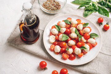 Italian caprese salad with cherry tomatoes, mozzarella, basil, balsamic sauce on a white table. Top view