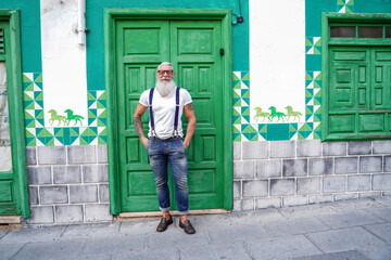 Full length photo of fashionable smiling senior man, positive emotions. Hipster guy wearing jeans and suspenders - obrazy, fototapety, plakaty