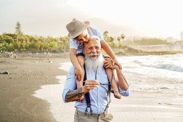 Happy kid playing on the beach with his grandfather, celebrating grandfathers day together,...