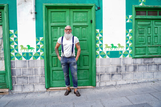 Full length photo of fashionable smiling senior man, positive emotions. Hipster guy wearing jeans and suspenders