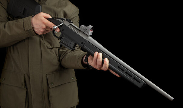 A man in a khaki jacket holds a bolt rifle with a reflex sight in his hands. Hunter with weapons. Dark back.