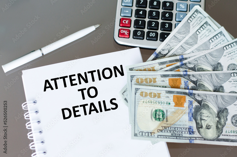 Poster attention to detail text on a notepad on a table next to a calculator and dollar bills