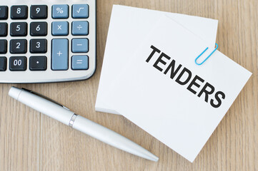 INVITATION FOR TENDER text on a card that is on a paper clip to a stack of notes sheets on a wooden table next to a pen and calculator