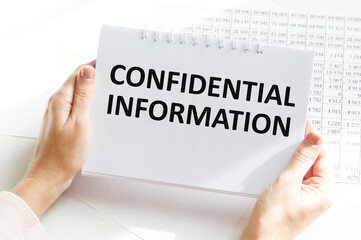 CONFIDENTIAL INFORMATION text on a notebook in the hands of a businessman on the background of reports, business concept