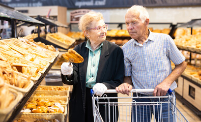 mature european couple shopping buns and bread in bakery section of supermarket