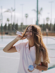 Mujer joven sonriente usando una raqueta de tenis en una pista de tenis al aire libre durante las vacaciones de verano