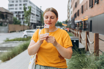 Fototapeta premium Happy attractive woman on the street having fun and eating ice cream. Young smiling girl dressed in yellow t-shirt holding ice cream. Food banner
