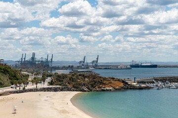 Drone shot of a sandy beach with Sines port in the background under a blue cloudy sky. Portugal