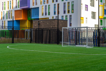 Soccer sports field with green synthetic artificial grass and gate next to a modern school building...