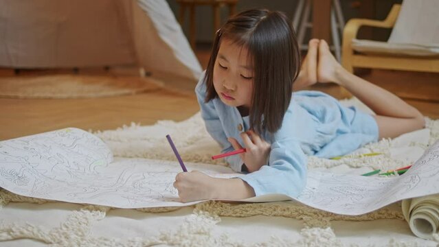 Talented little Asian Girl Paints on Paper, Using Color Pencil , Set Create a Colorful Emotional Painting With Paints. Preschool Girls are Engaged in Creativity at Home on Floor.