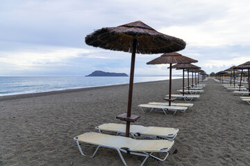 Empty beach with sun loungers and umbrellas in the early morning and a cloudy sky. Crete Greece. High quality photo