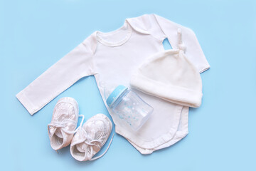 accessories for a newborn on a blue background - cap, bodysuit, booties, milk bottle