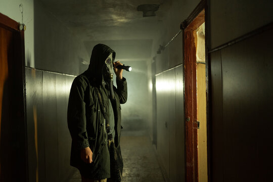 Man in respirator gas mask with flashlight inside of abandoned building in dark. Cyberpunk postapocalypse fantasy horror scene, or air pollution