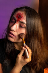 Obraz premium Close-up of a young woman putting on halloween makeup with a zombie image with a wound on her forehead