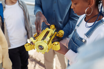 Close up of young black girl holding robot model during engineering class outdoors with teacher...