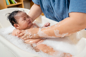 Fototapeta premium Single mother uses water to wash the soap off her body, and her infant daughter's face, After taking a shower at the end of the day, Mother bathed the girl during the day due to the hot weather.