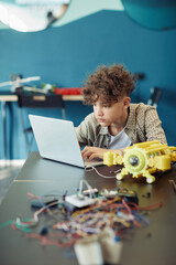 Vertical portrait of young curly haired boy using laptop in school during engineering class and...