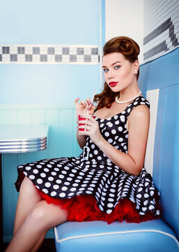 Retro (vintage) portrait of beautiful young woman sitting in cafe and drinking beverage. Pin up style portrait of young woman in dress