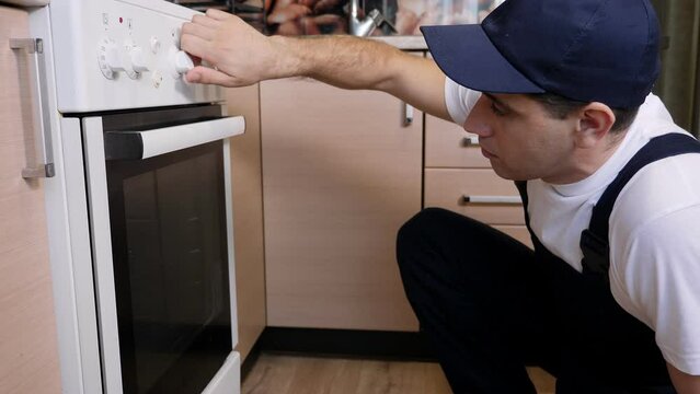 A Man From The Maintenance Service Repairs A Gas Stove In The Kitchen.